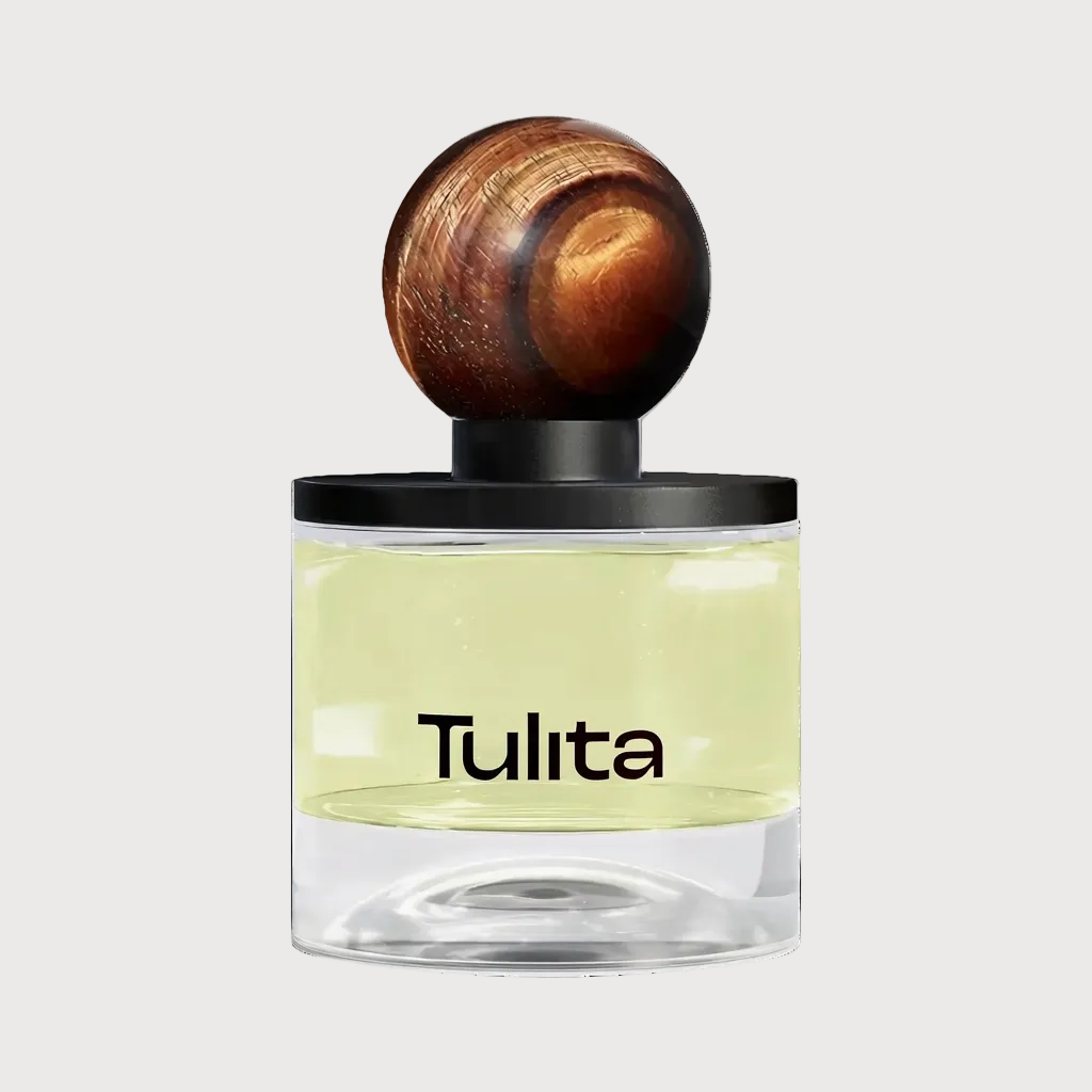 A Tulita fragrance bottle with a clear glass body showing pale yellow liquid, a black collar, and a round wooden stopper on a light gray background.