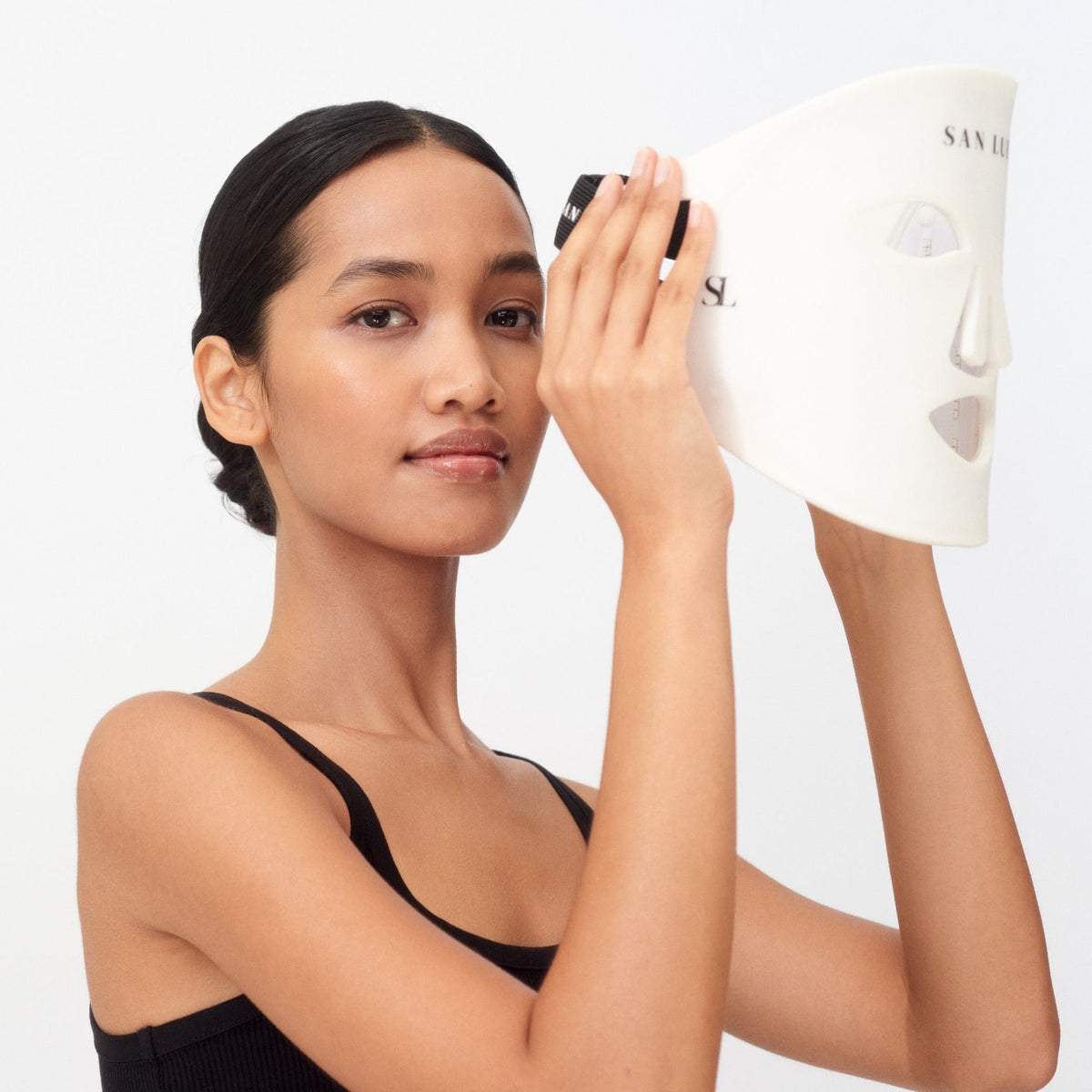 Woman holding a skincare product with a plain background