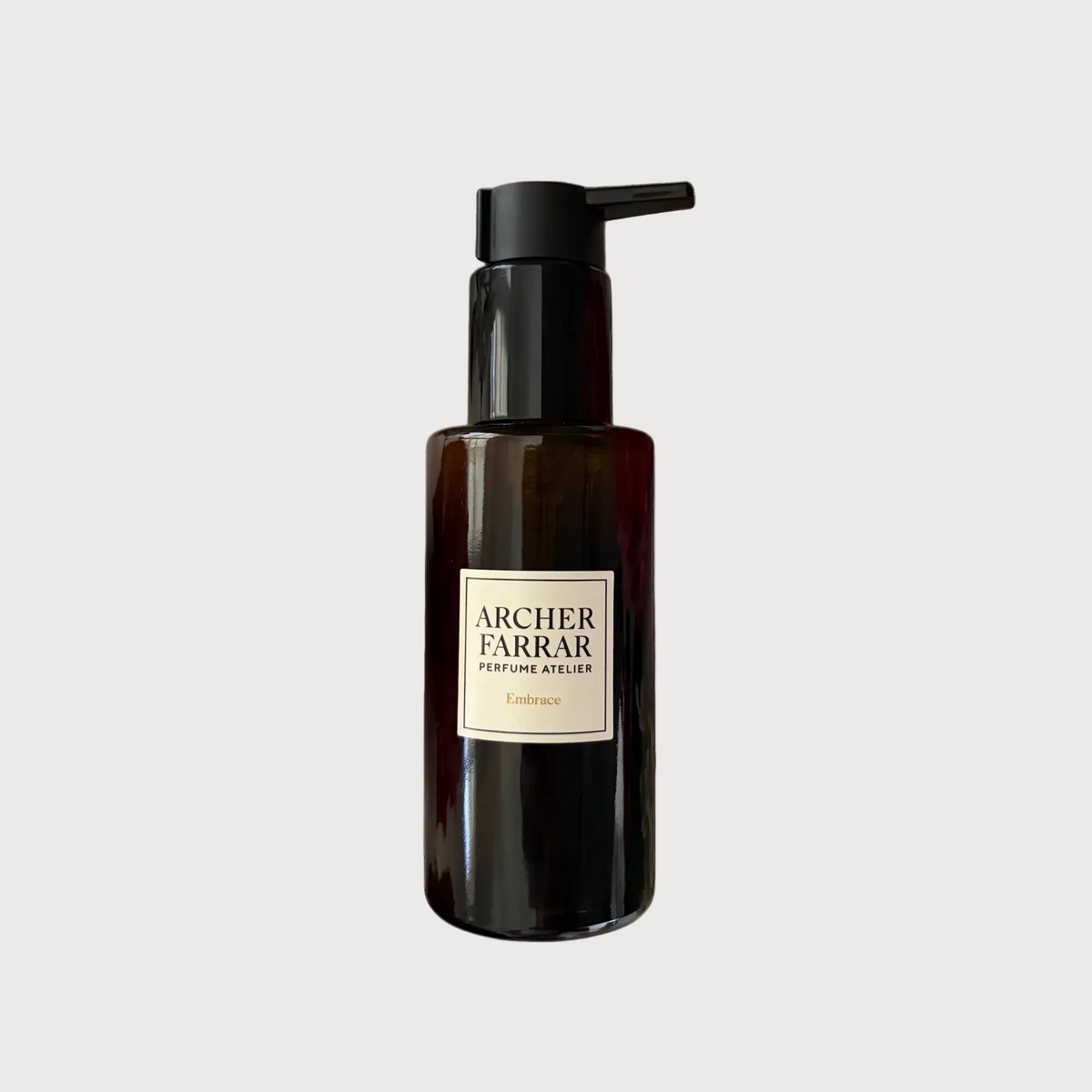 A dark amber glass bottle with a black pump dispenser and a cream-colored label reading 'ARCHER FARRAR PERFUME ATELIER' and 'Embrace', set against a plain white background.