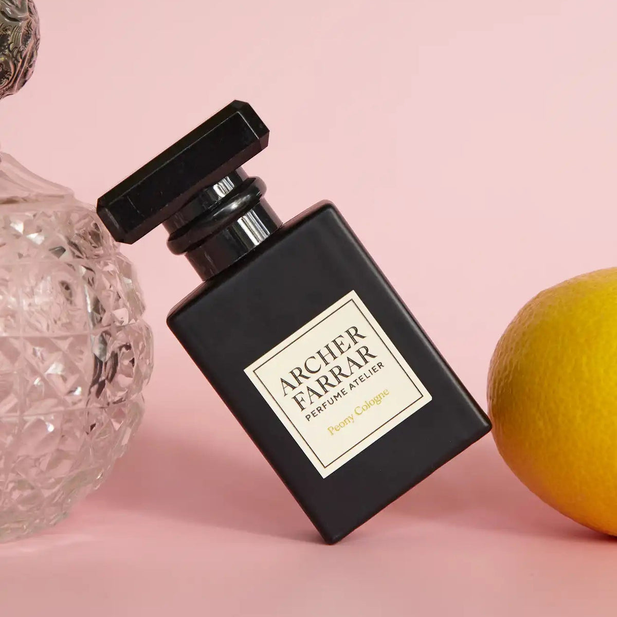 Black Archer Farrar perfume bottle on a pink background with decorative elements.