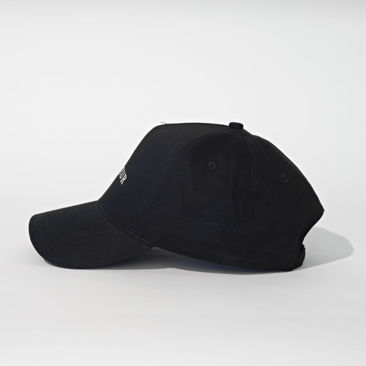 A black baseball cap with a small white embroidered logo on the side, photographed from a three-quarters angle against a light gray studio background.