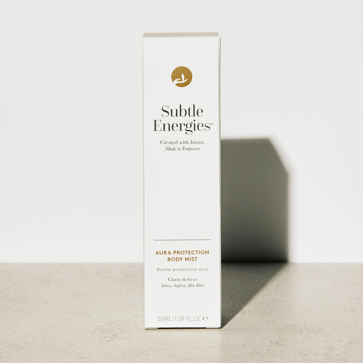 A tall white rectangular box for Subtle Energies Aura Protection Body Mist, standing upright on a light beige surface against a white wall with a soft shadow.