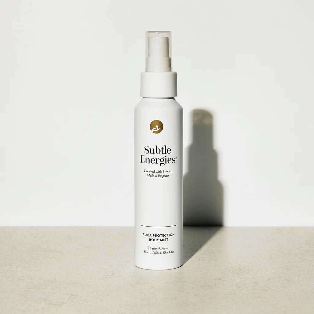 A white spray bottle of Subtle Energies Alpha Protection Body Mist with a clear cap, standing on a light beige surface against a white background with a soft shadow.