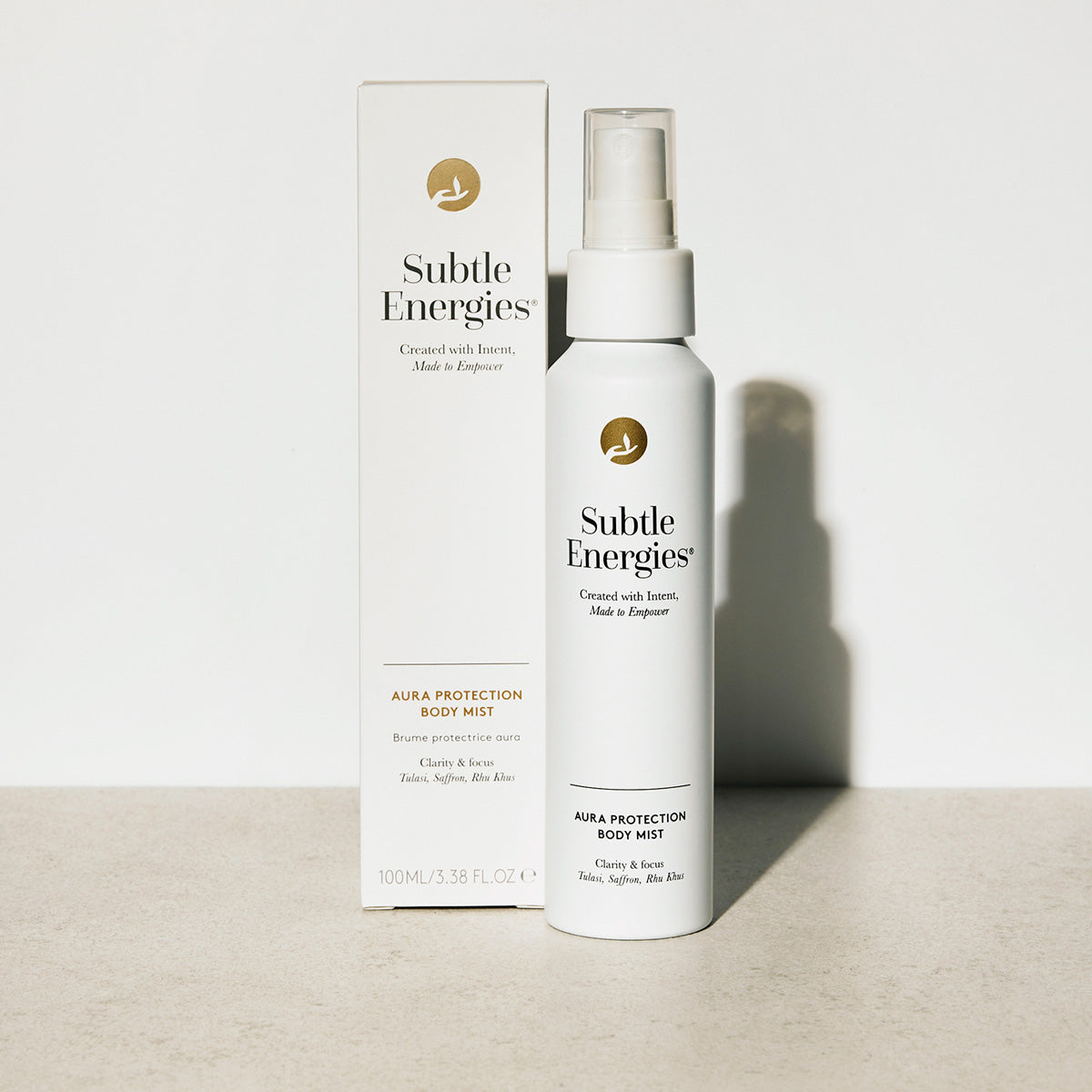 A bottle of Subtle Energies Aura Protection Body Mist next to its white packaging box, set on a light beige surface against a white background with a soft shadow.