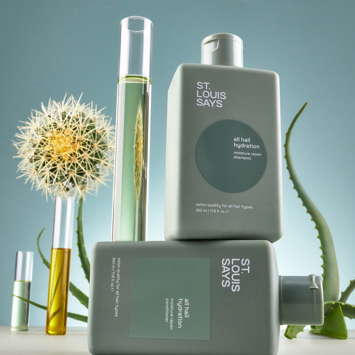 Bottle of St. Louis Says hair product with a plant and flower on a light blue background