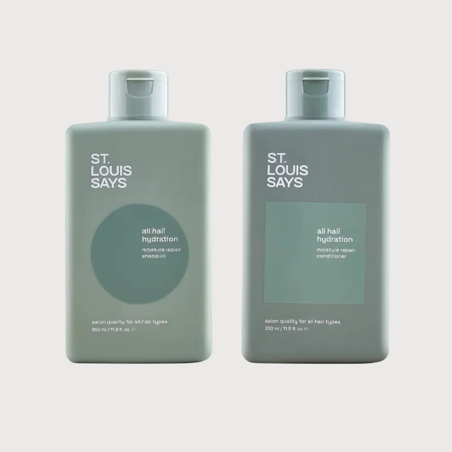 Two St. Louis Says hair care bottles in a muted sage green color, shown side by side against a light beige background.
