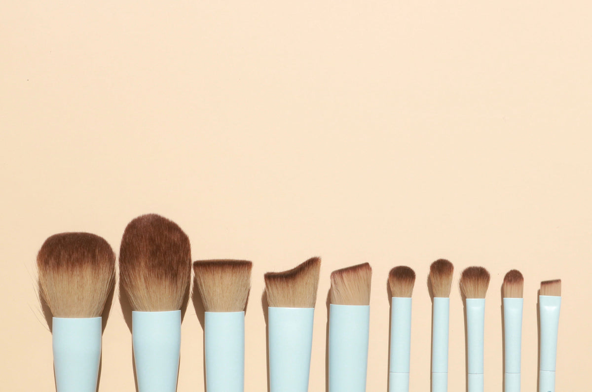 Set of makeup brushes with wooden handles and white bristles on a beige background