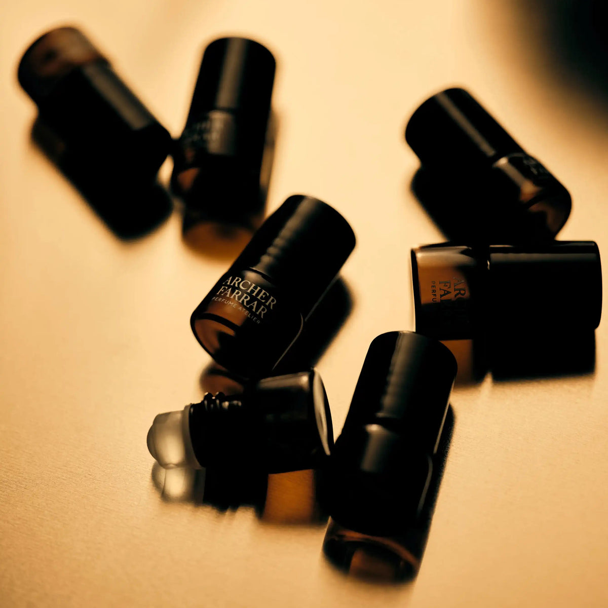 Several small black cosmetic tubes or bottles with caps off, arranged on a warm beige surface. One tube shows the text 'SHEER TO BE SURE'.