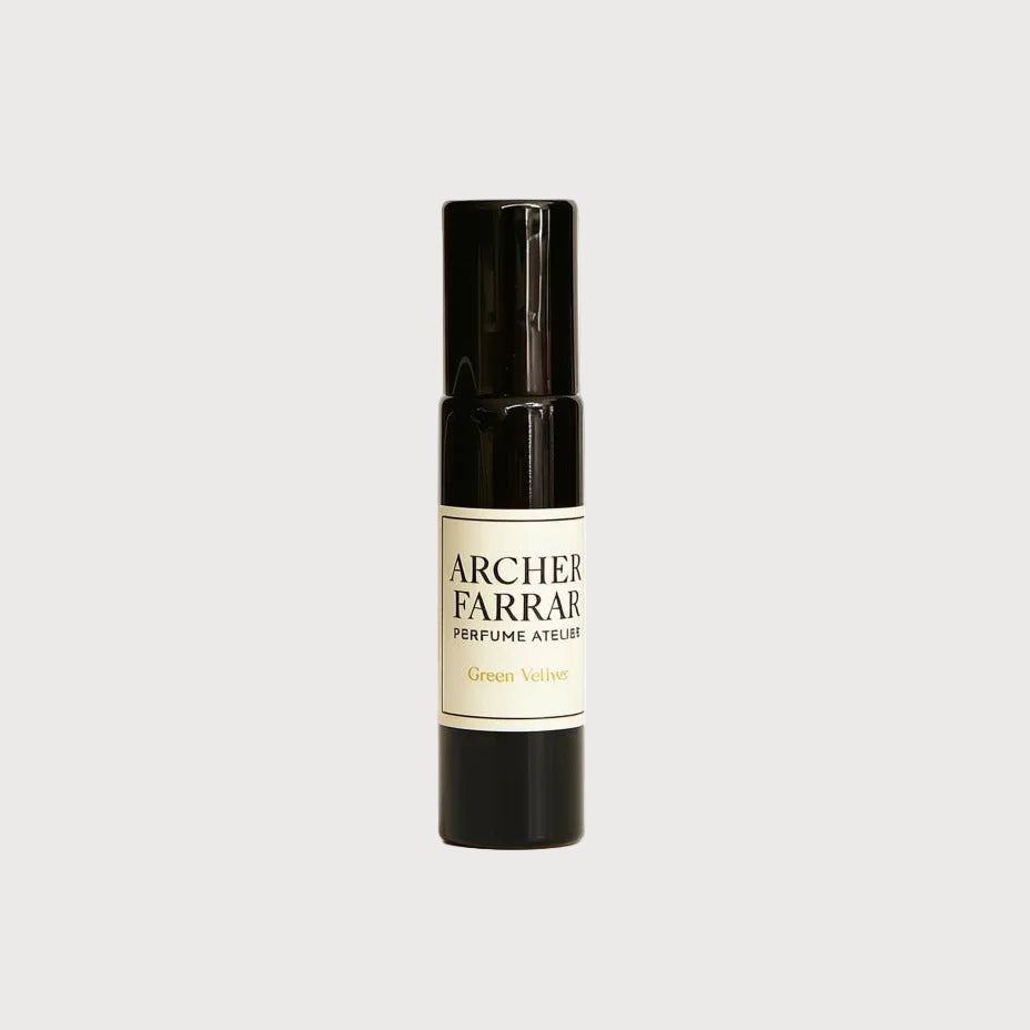 A single small cylindrical perfume atomizer bottle by Archer Farrar, featuring a glossy black body with a cream-colored label and black text, set against a plain white background.