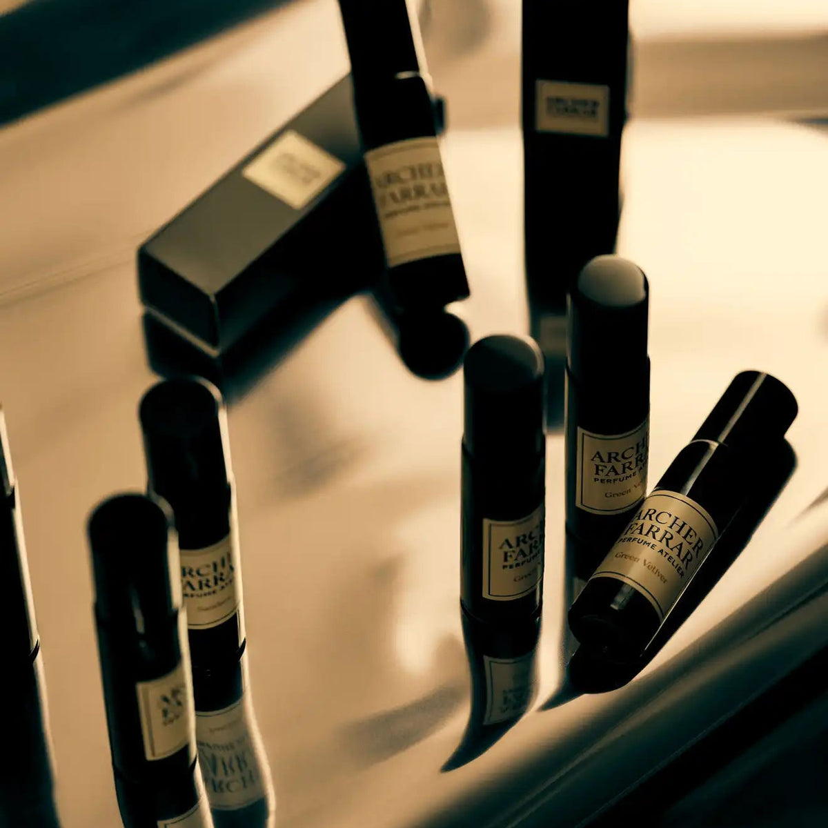 Several small black roll-on bottles and matching black boxes with cream labels are arranged on a glossy reflective surface. The labels read 'ARCHITEC THERAPEUTIC' and '10 ML'.