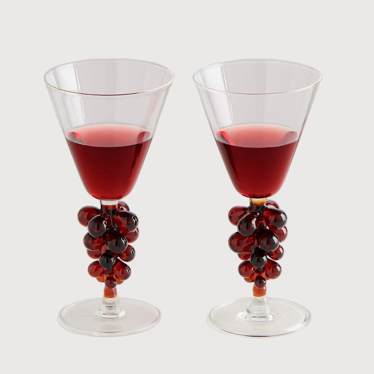 Two glasses with red liquid and decorative grapes on a white background