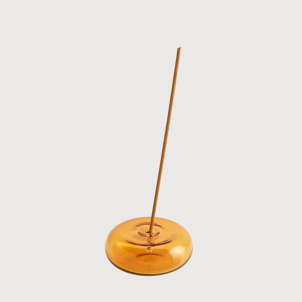 Incense stick on a metallic disc against a light gray background