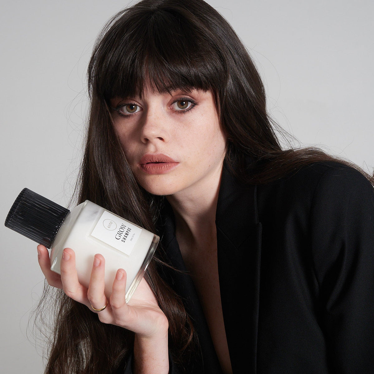 Woman holding a shampoo bottle against a plain background