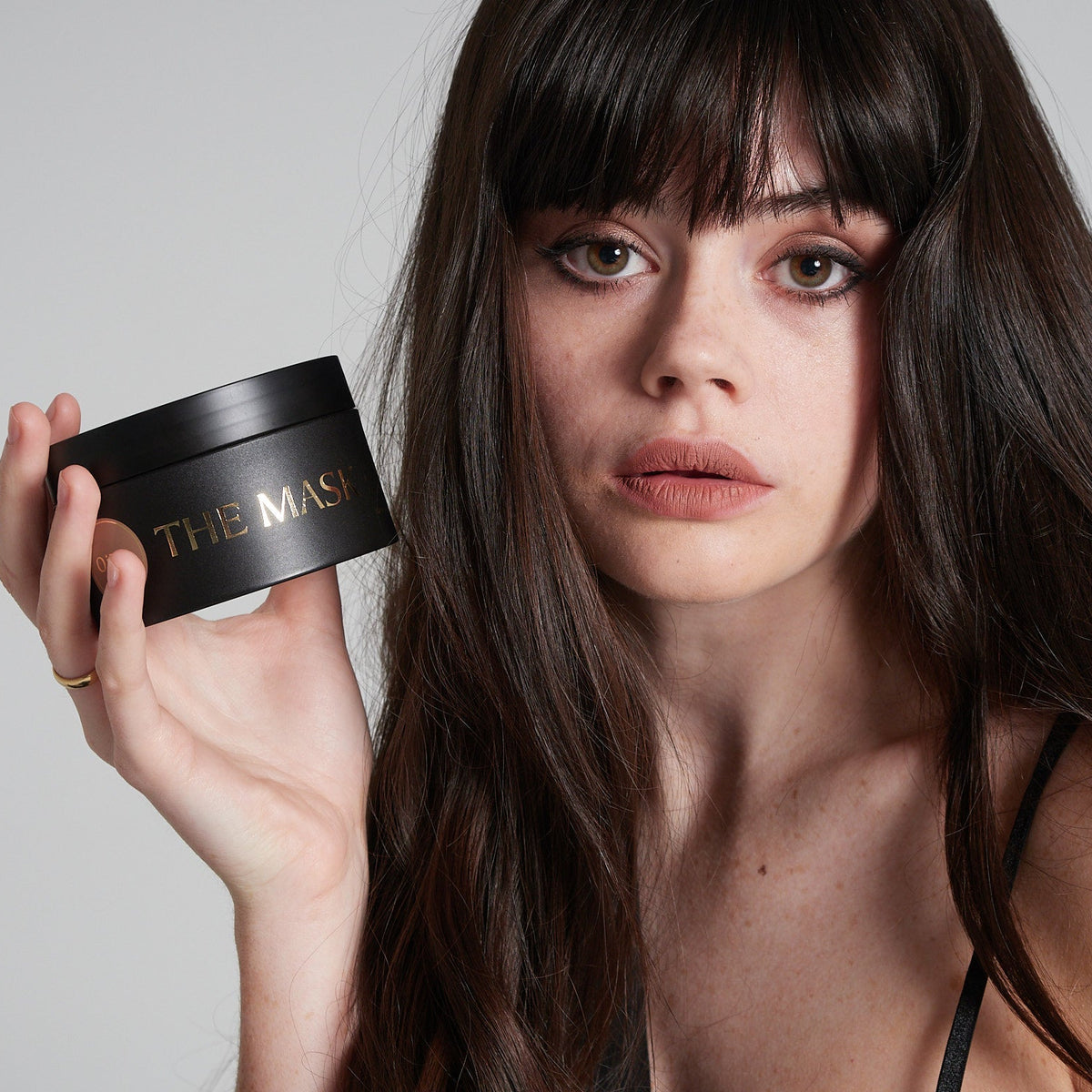 Woman holding a black container labeled 'THE MASK' against a plain background