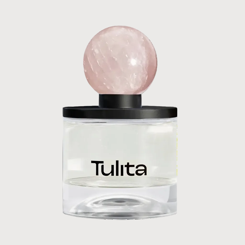 A Tulita brand diffuser with a clear glass base, a black collar, and a round pale pink stone top, shown on a light gray background.