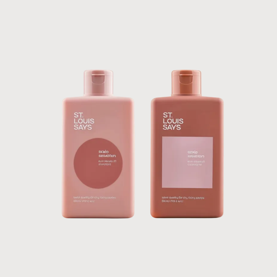 Two rectangular bath and body products from St. Louis Says, one in dusty pink and one in terracotta, standing side by side on a light beige surface against a cream background.