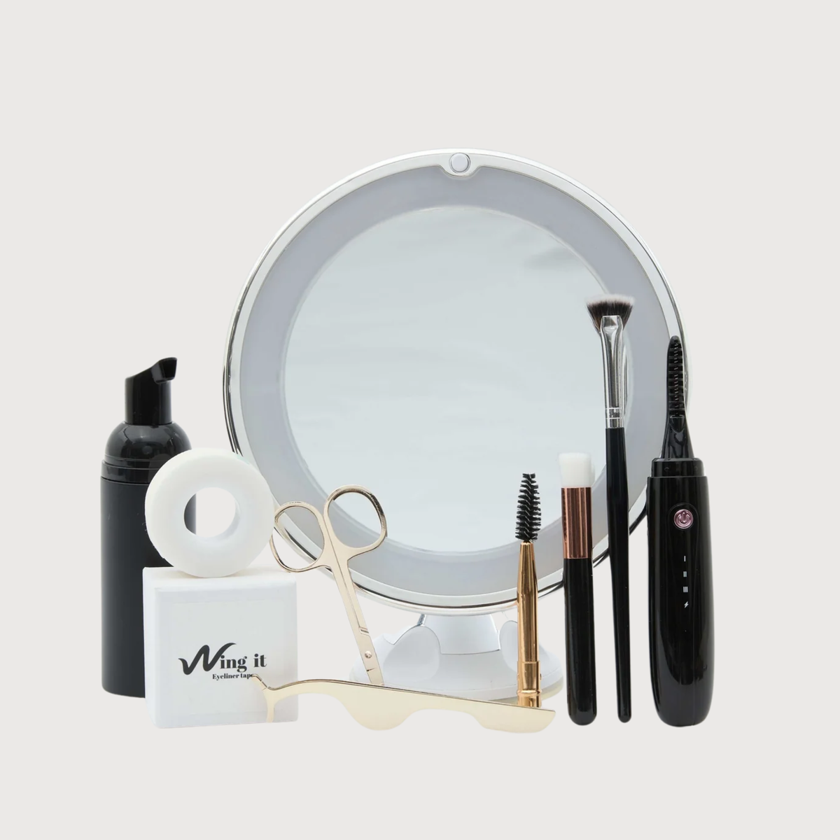 Collection of makeup and beauty tools including a mirror, brushes, and bottles on a light gray background.
